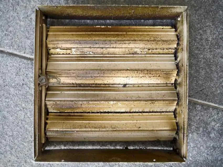 A ceiling diffuser's blades, the gaps between them filled with brown grease and grime