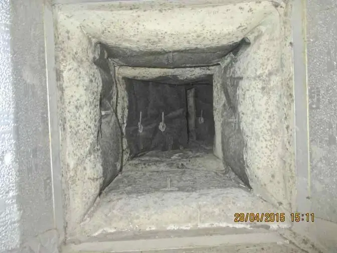 Looking into a square duct opening, every wall coated in grey dust